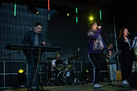 A dark stage lit by coloured tubes, keys on the left and drums behind
